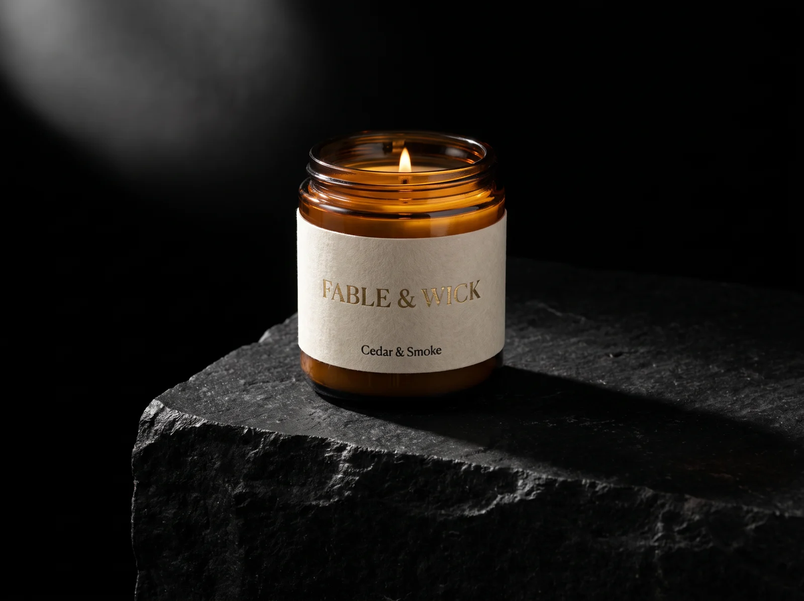 Amber glass candle jar with a cream felt-textured wrap label, the brand name in gold foil