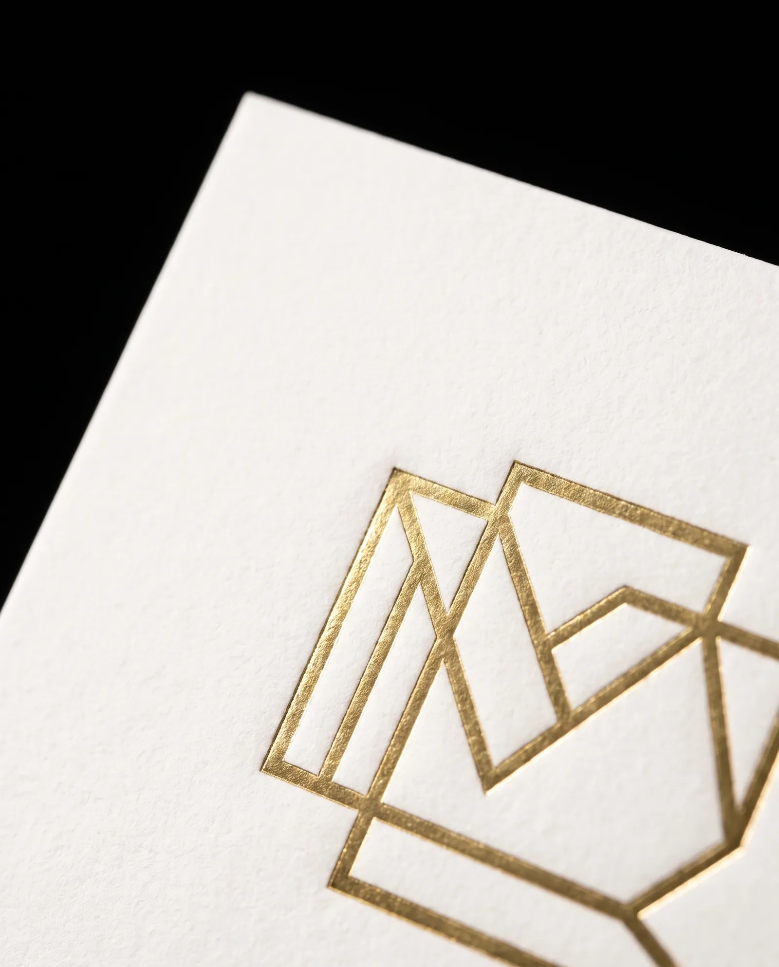 Macro of a gold hot foil geometric monogram pressed into white cotton card stock