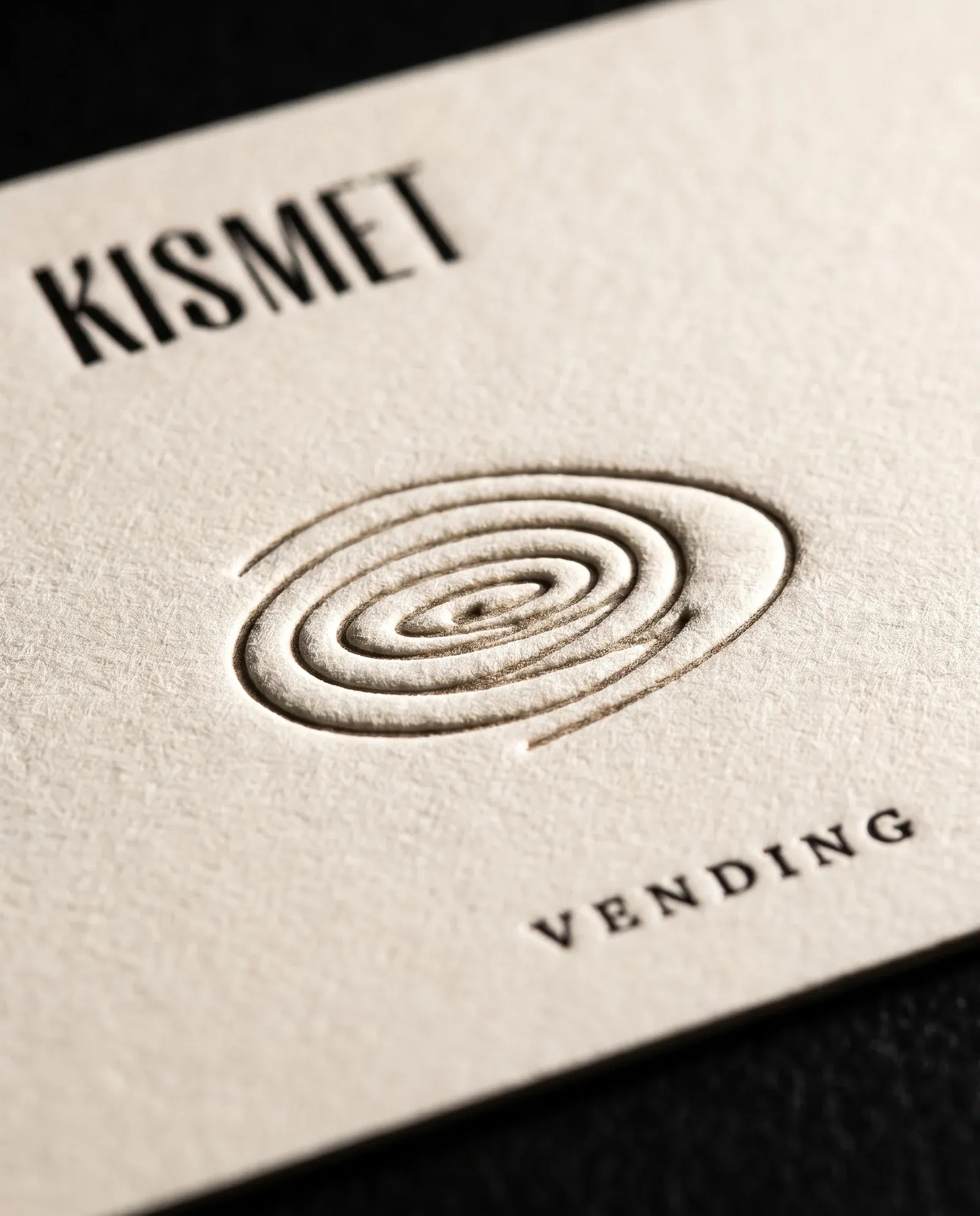 Kismet Vending card: spiral mark blind debossed into cream cotton beside letterpress type