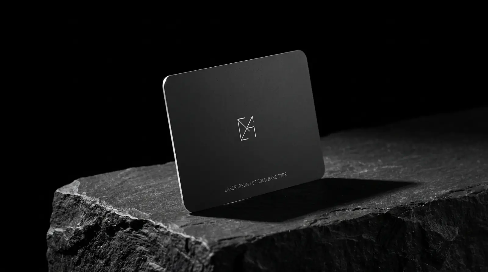 Matte black stainless steel business card standing on a slate plinth, monogram laser engraved to bright steel