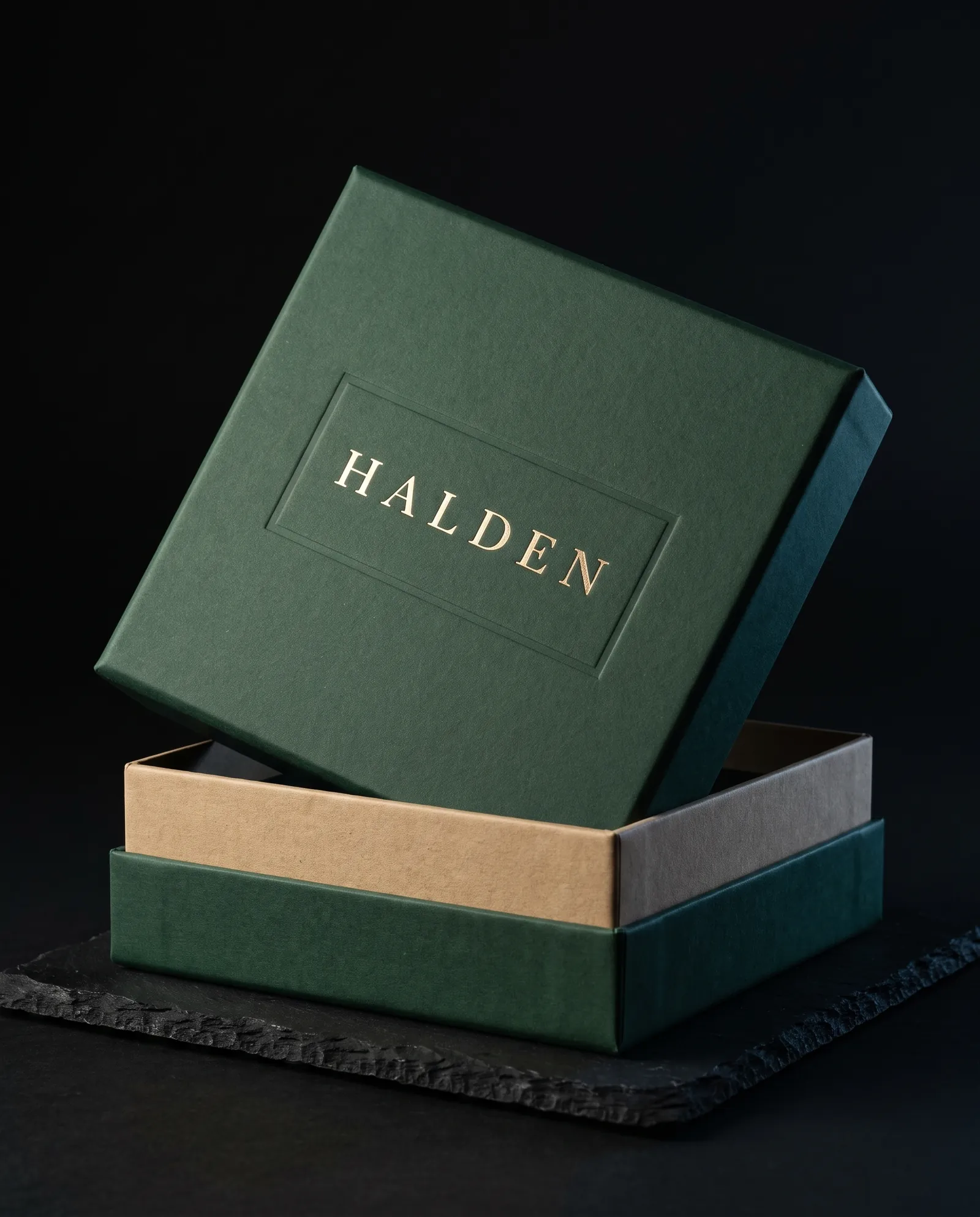 Green wrapped rigid box with the lid lifted, showing the chipboard wall and a foil wordmark inside a debossed border