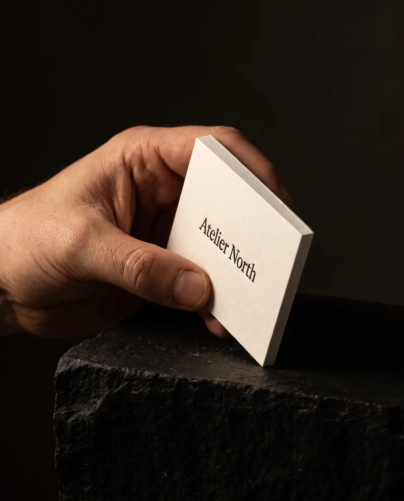 Hand holding a thick natural white cotton business card with black letterpress name, dark studio