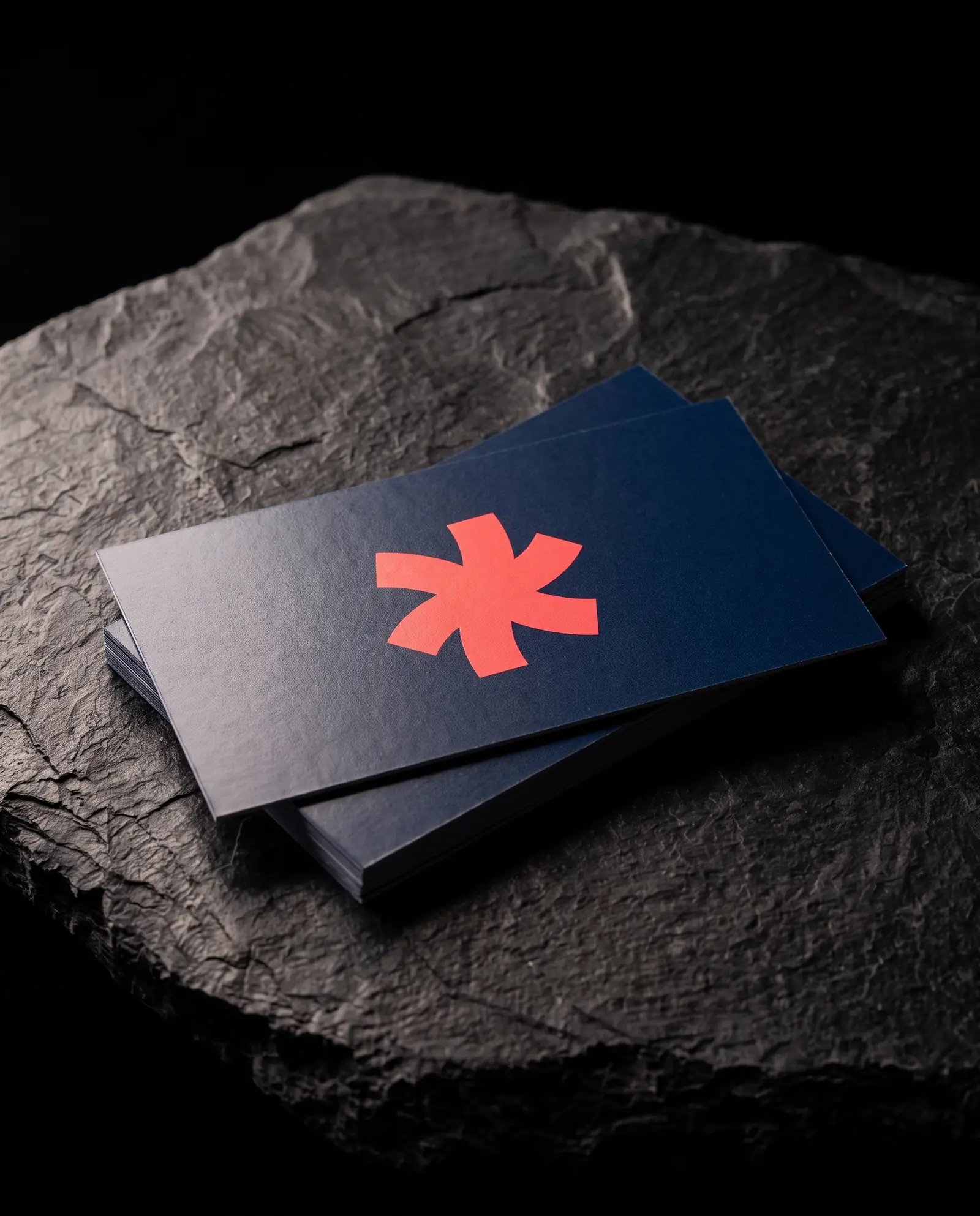 Stack of navy silk-laminate business cards with a coral Print Peppermint mark and a soft satin sheen on black slate