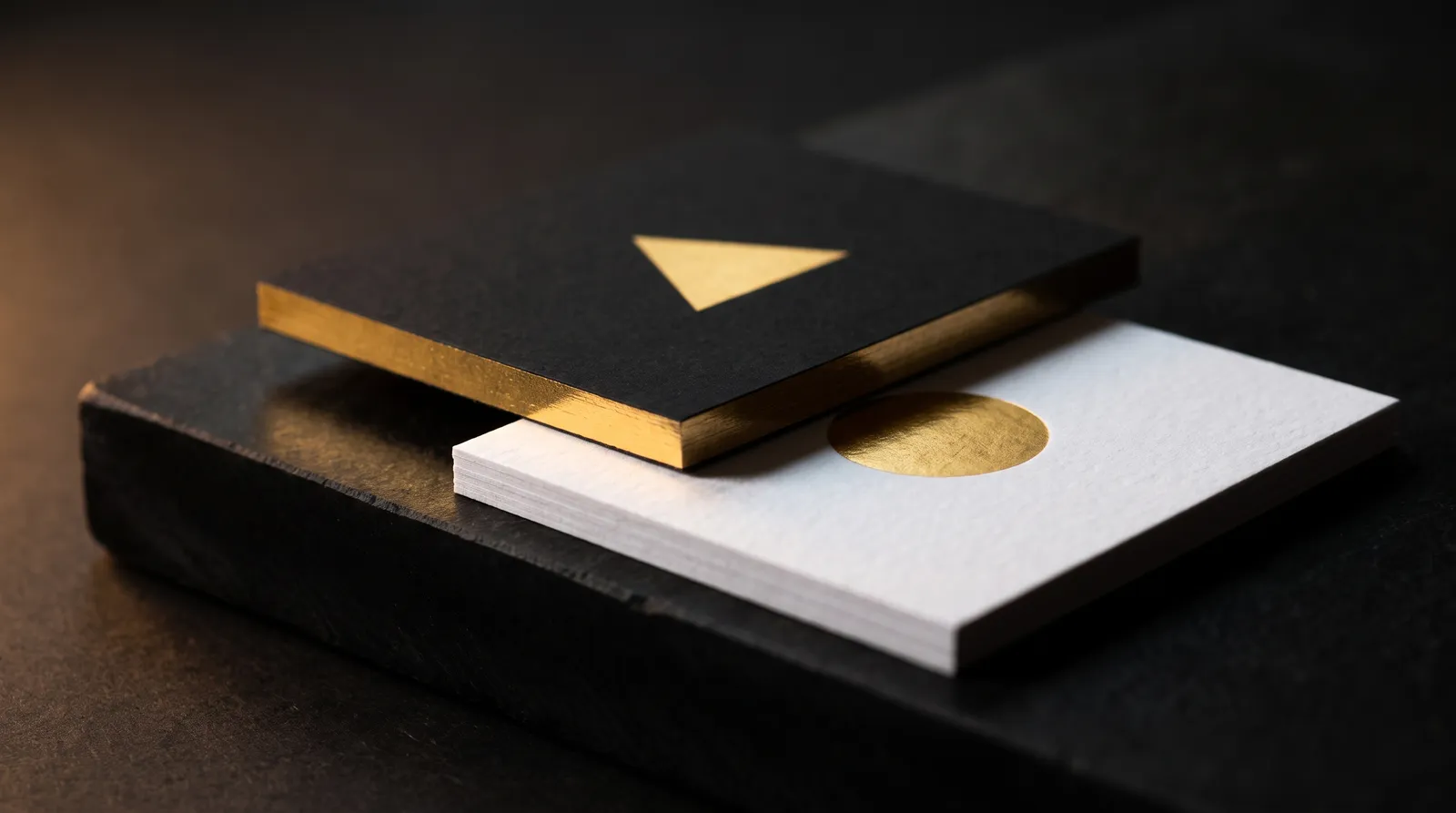 Black business card with gold foil face and gold foiled square edges resting on a white cotton card with gold hot foil