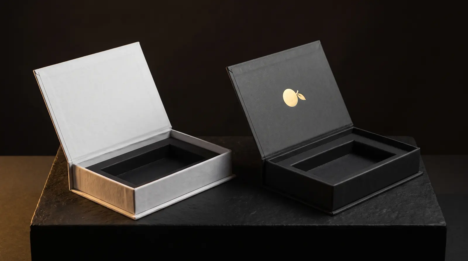 White unprinted magnetic box prototype beside finished charcoal box with gold foil, same tray