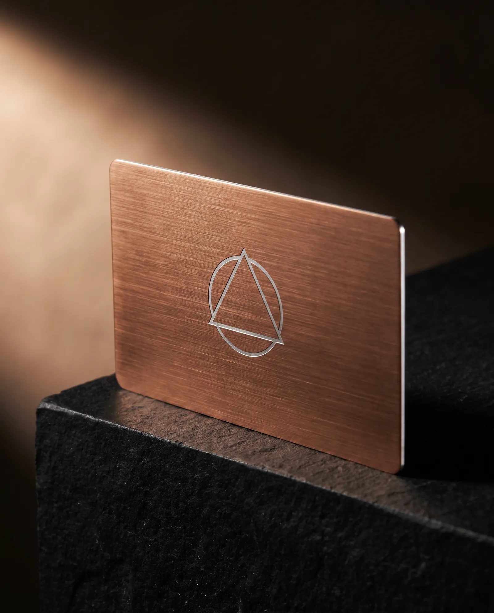 Brushed copper-tone PVD stainless steel business card with an engraved logo showing bright steel
