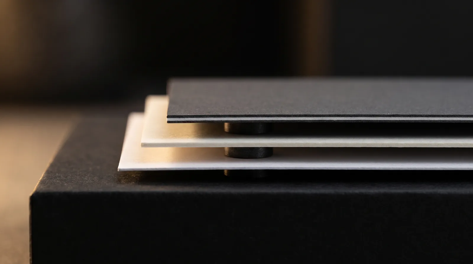 Side profile of three thin business cards, charcoal soft-touch edge showing a fine white paper core