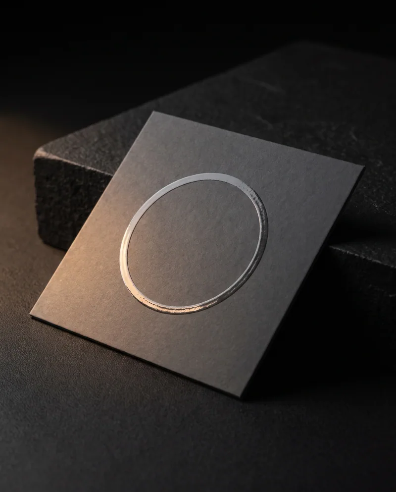 Clear spot UV ring logo catching light on a charcoal soft-touch square business card