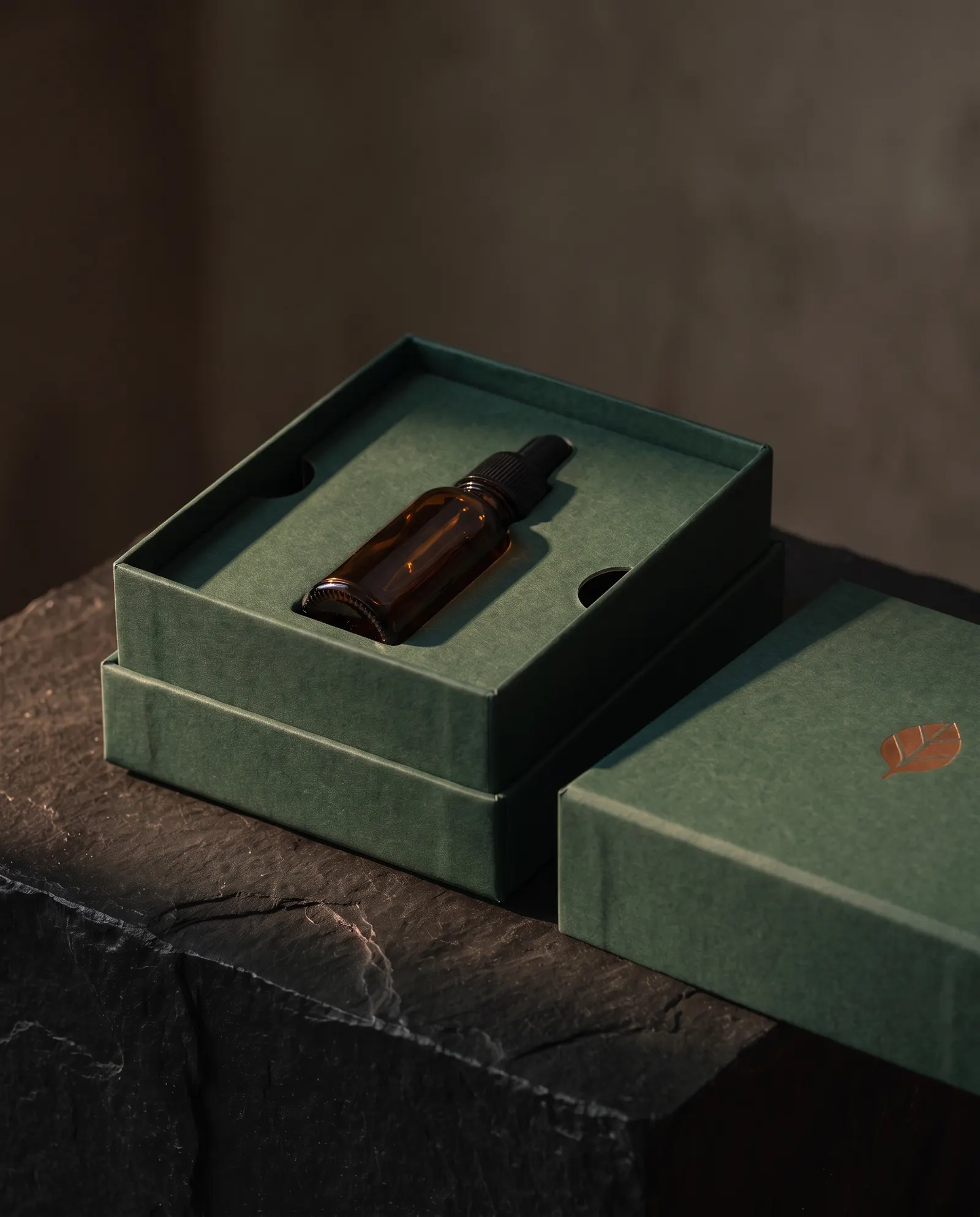 Open green rigid box with paperboard tray holding an amber dropper bottle, lid beside it