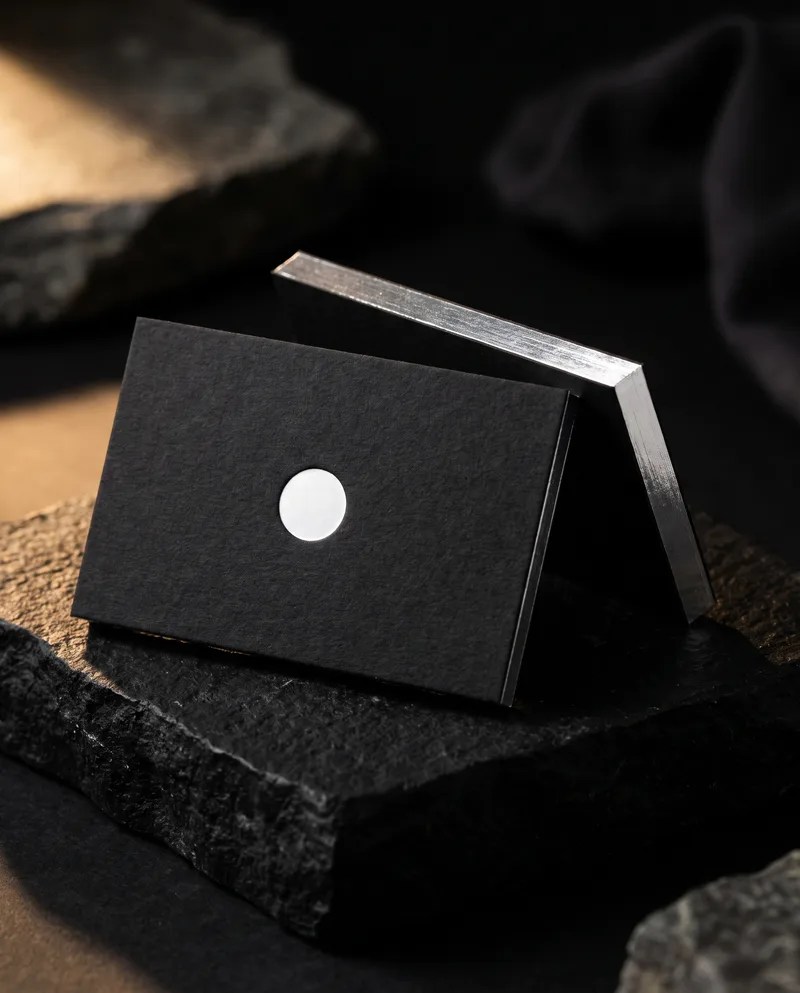Thick black cotton business card, white foil debossed circle, silver edge foil, square corners on stone