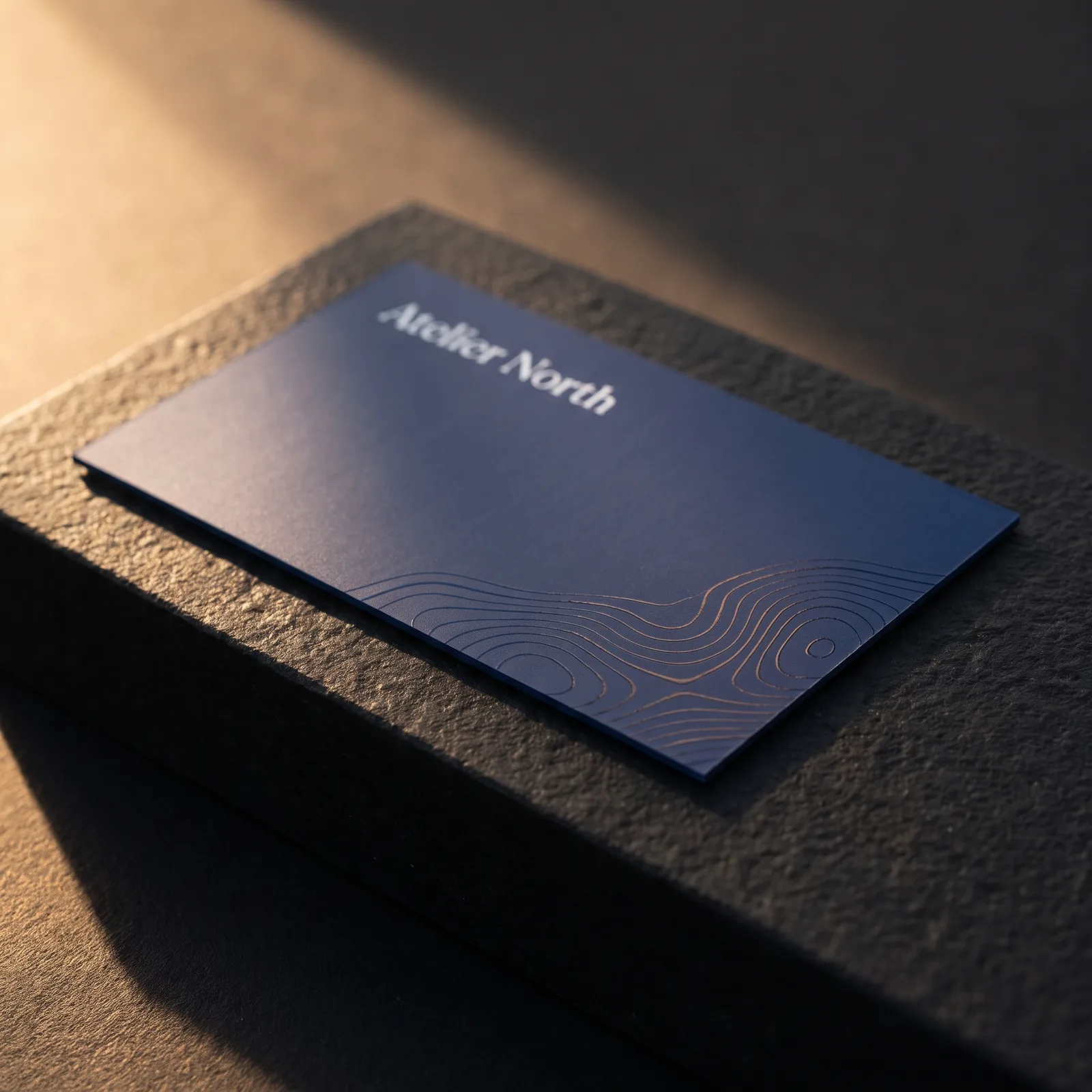 Navy silk business card with flat clear spot UV topographic lines glinting in one corner