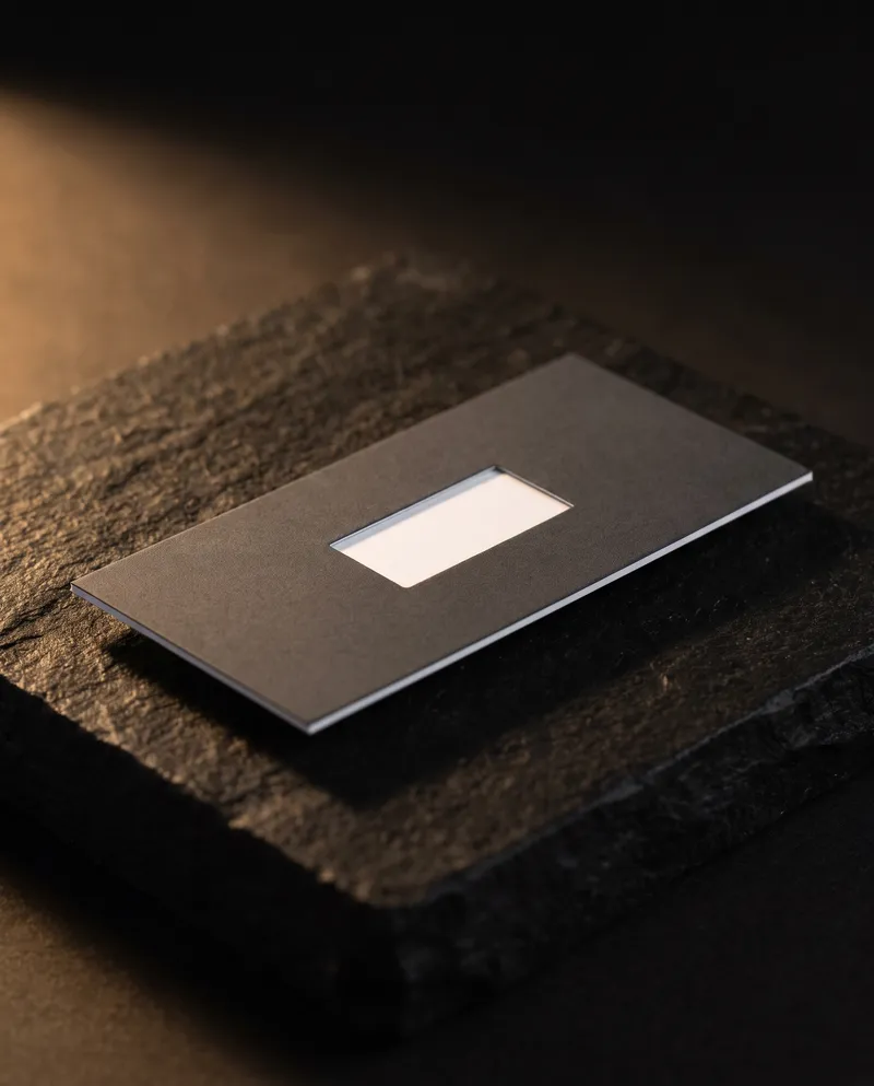 Charcoal soft-touch mini business card with a white wordmark, its matte laminate absorbing the light