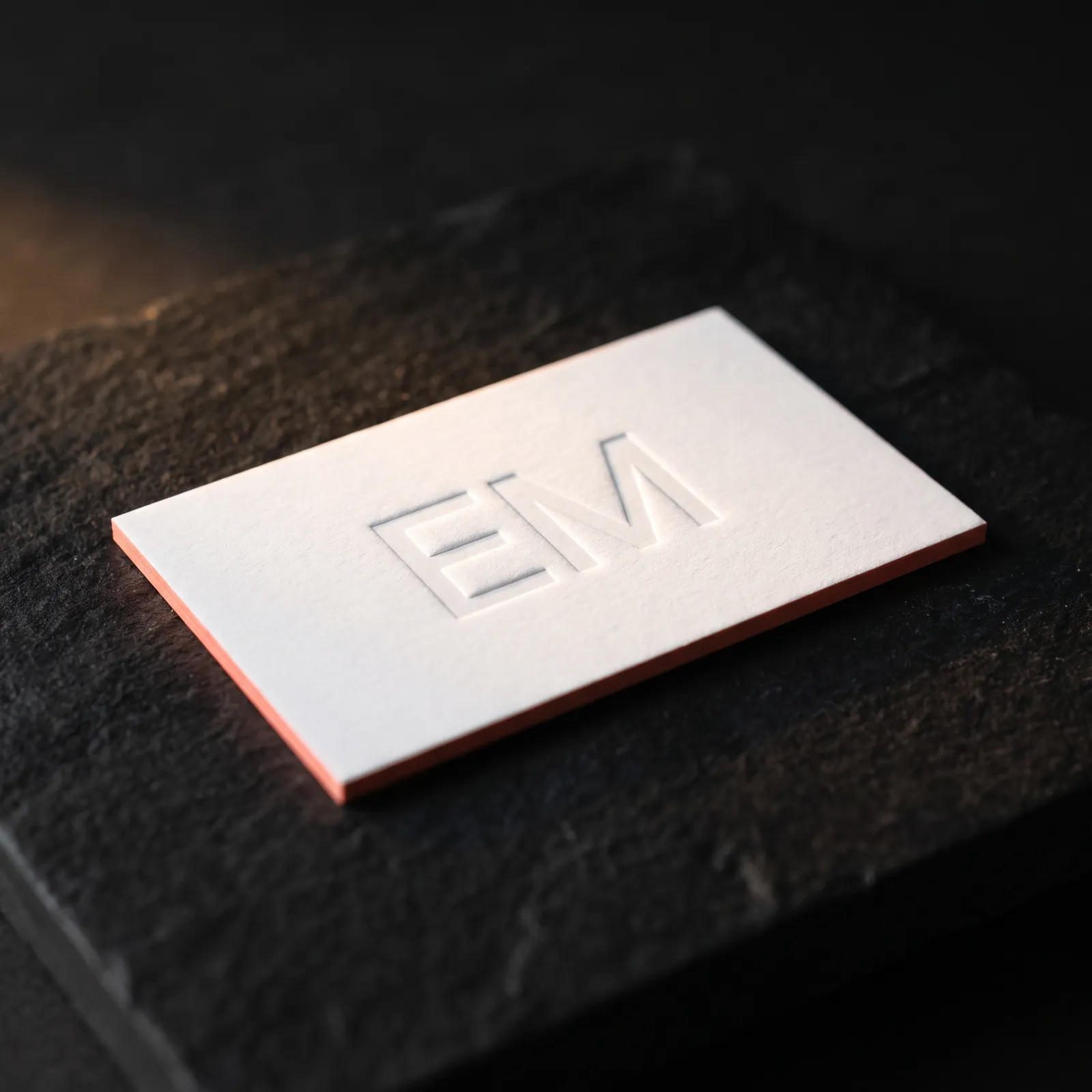 32pt white cotton business card with blind debossed EM monogram and coral painted edges