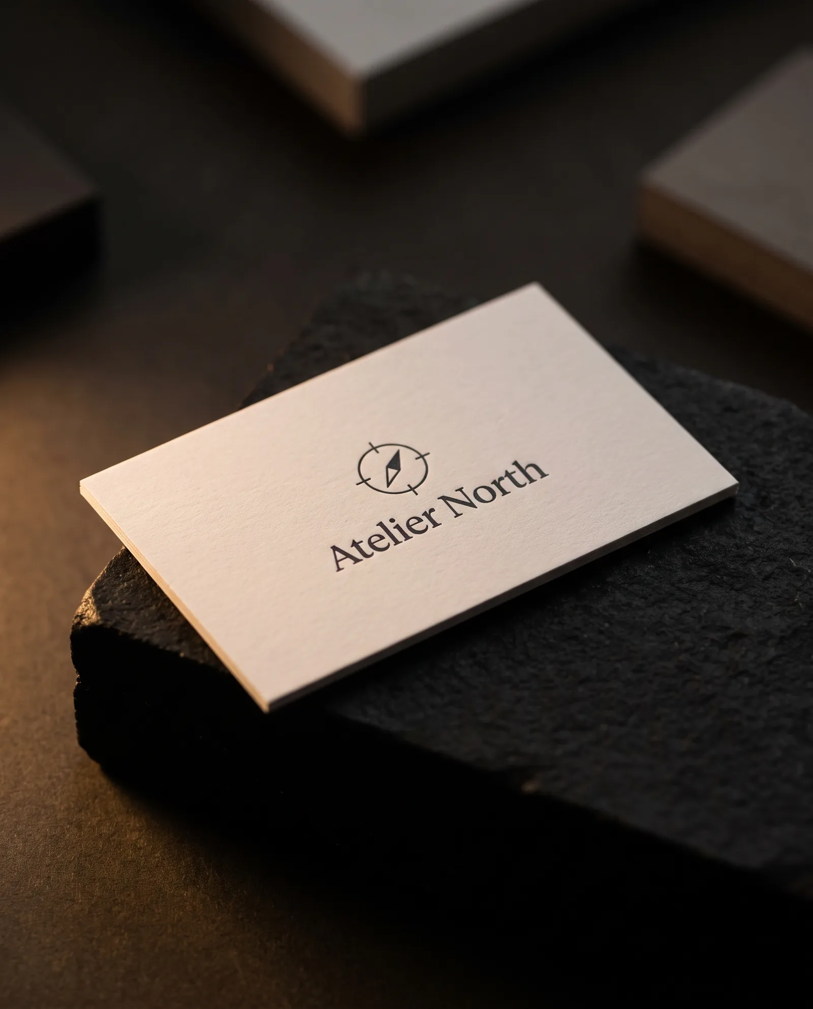 Concept rendering of a matte off-white business card with charcoal Atelier North wordmark and compass mark