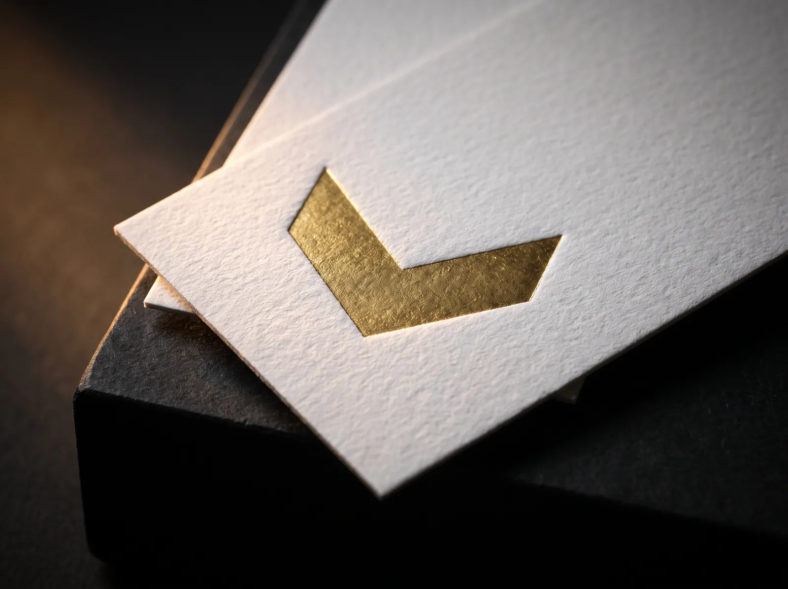 Macro of gold foil stamped into white cotton paper, light catching the edge of the slight bite