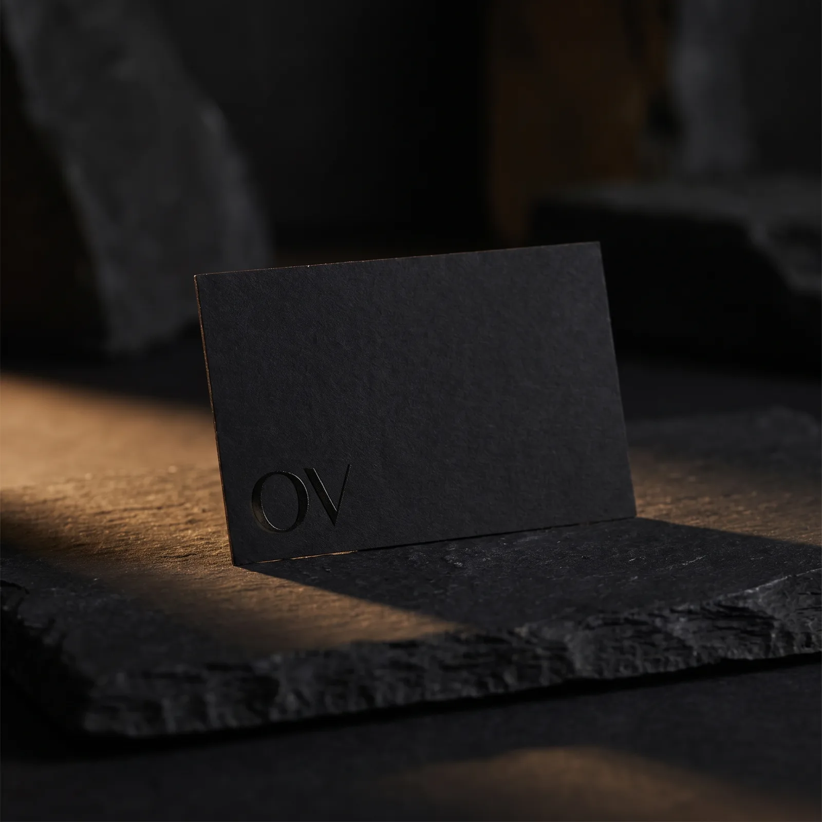 Black soft-touch business card with black-on-black raised gloss monogram visible as subtle sheen