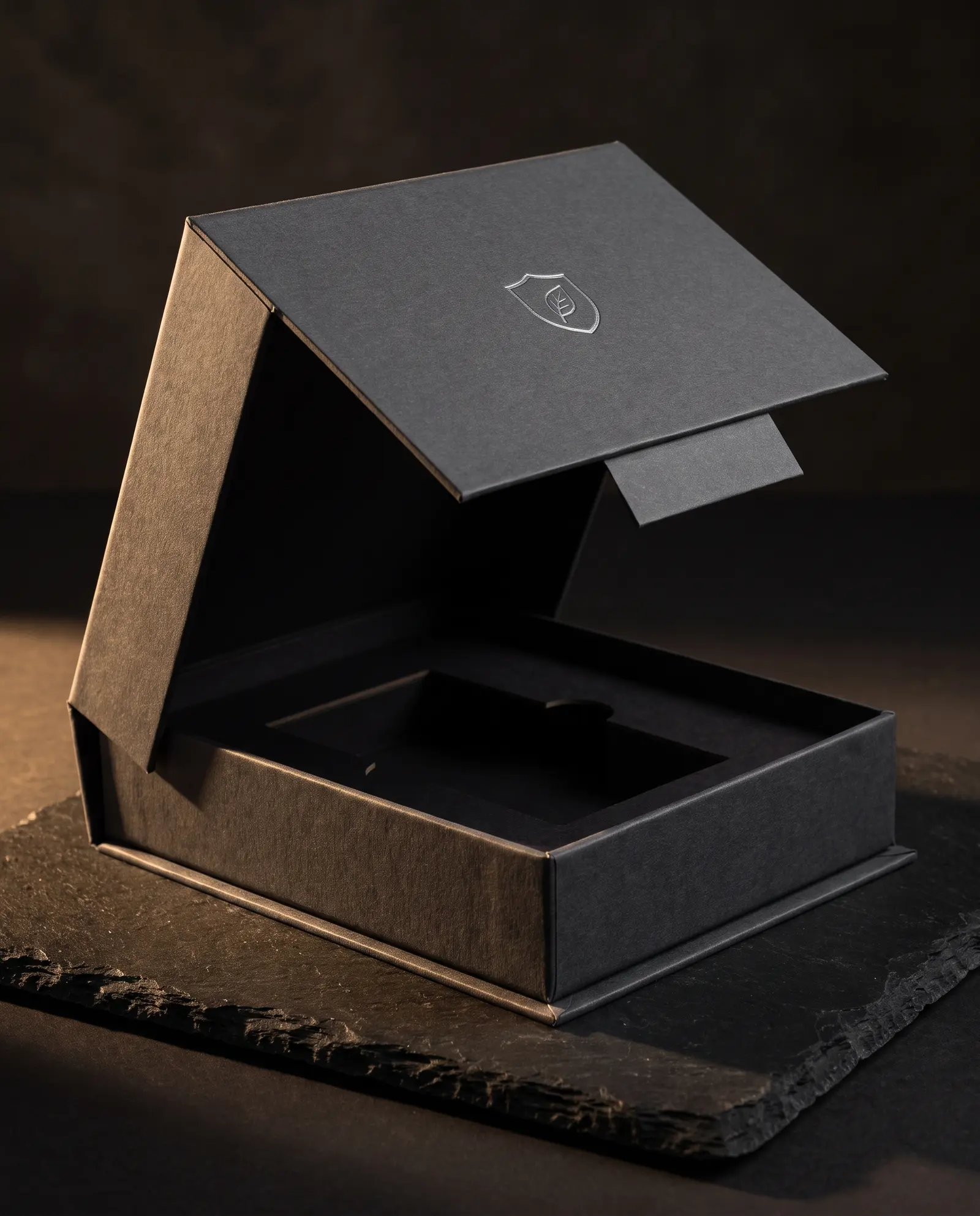 Charcoal uncoated magnetic gift box open on black stone, silver foil crest, paperboard tray