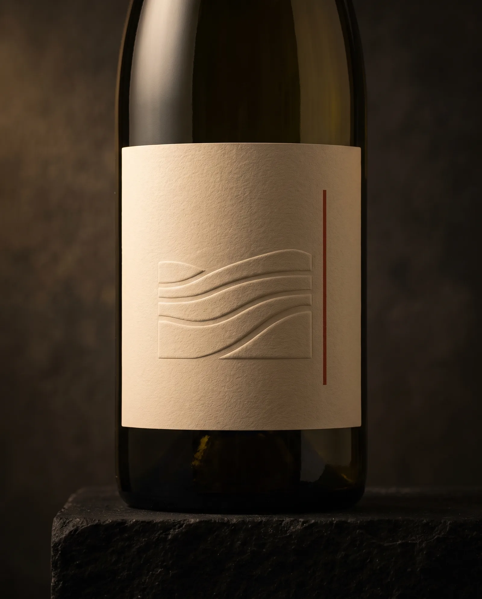 Wine bottle with an oat-coloured cotton label embossed in four stepped levels like terraced hills, raking light showing each step.