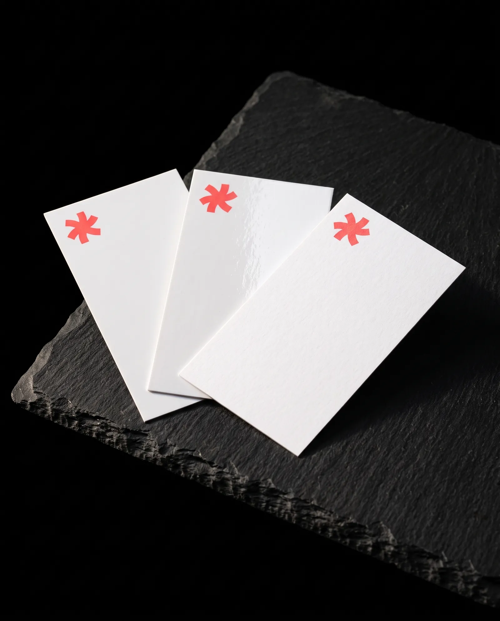 Three white Standard business cards fanned on black slate in matte, high gloss and uncoated, each with a small coral Print Peppermint mark
