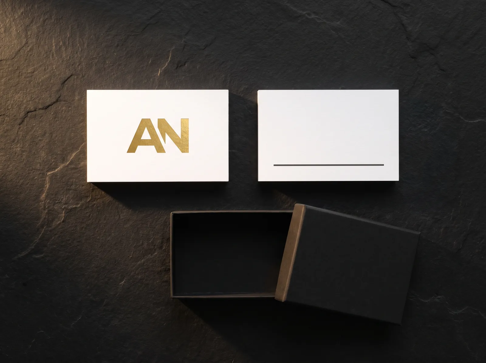 White cotton card with a gold foil monogram, its printed back and a black card box in a flat lay
