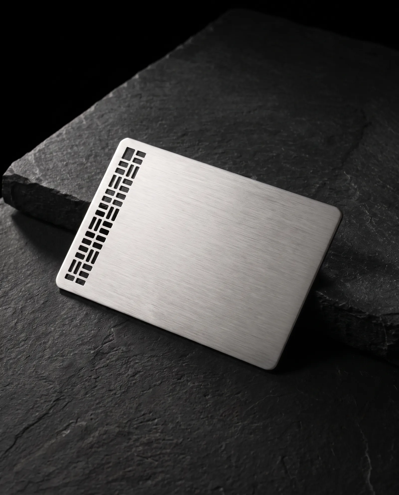 Brushed stainless steel business card with a laser-cut pattern casting shadows on stone