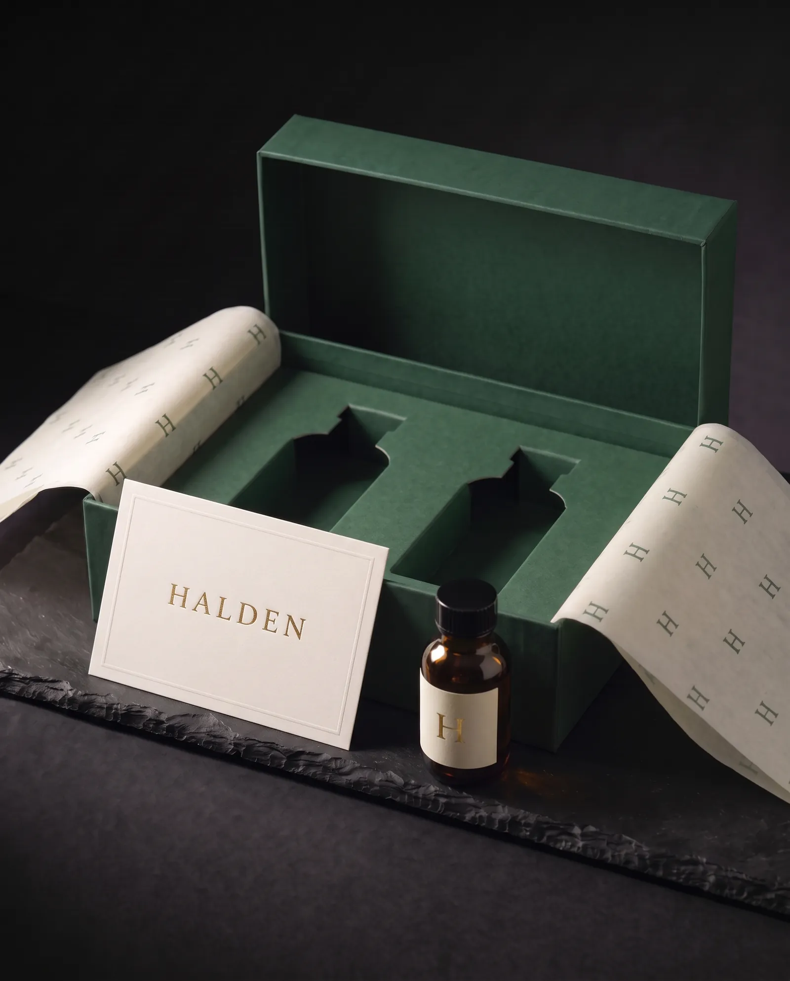 The insert card and an amber bottle with a foil label in front of the open box and its die-cut tray
