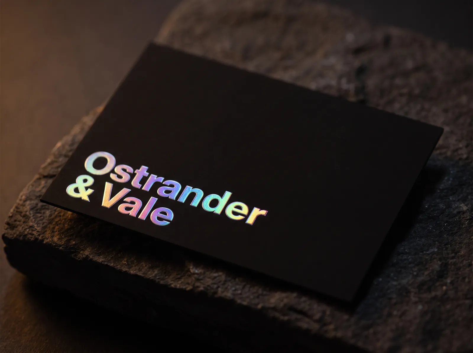 Holographic foil business card on black soft touch, rainbow foil shifting colour as the camera moves