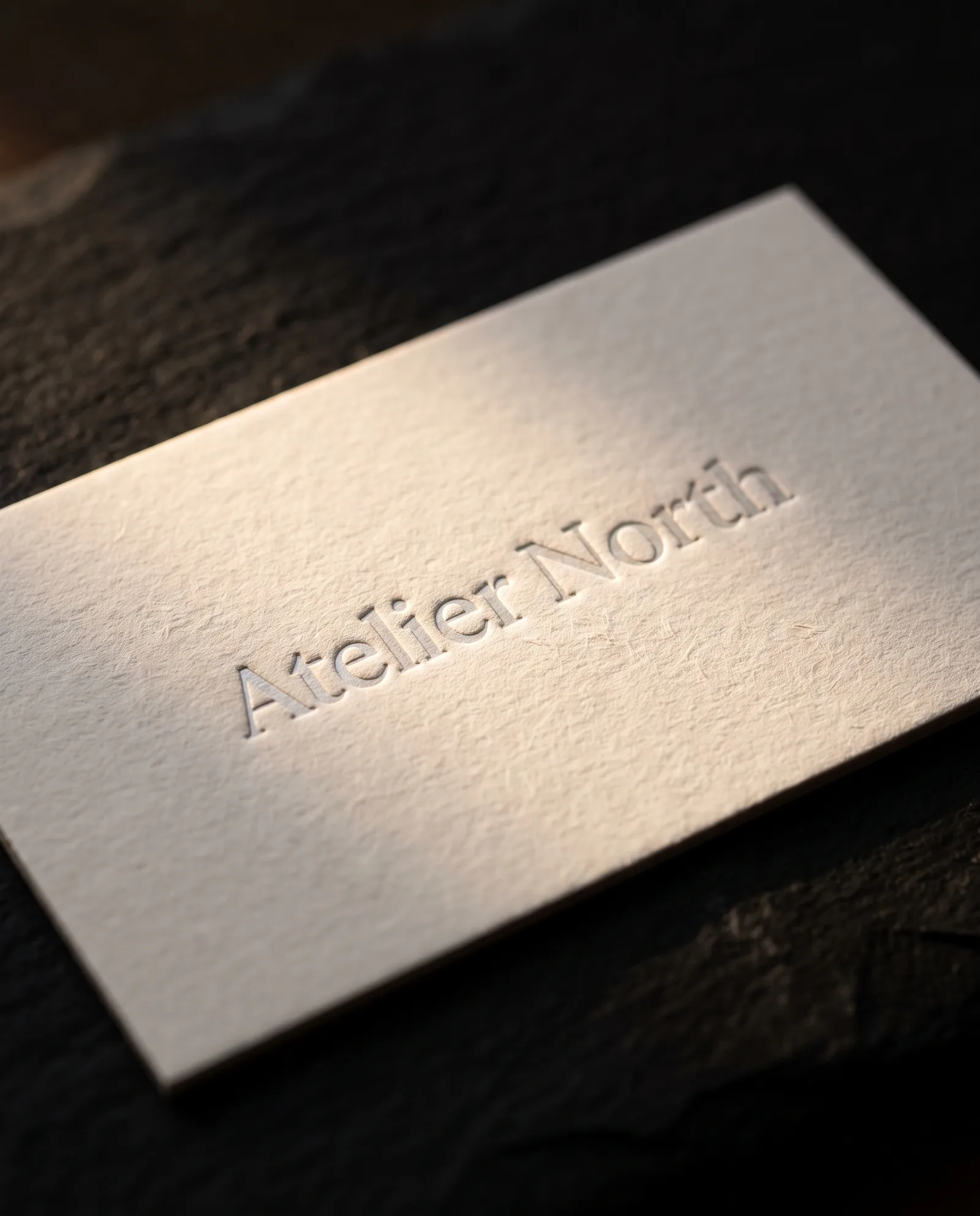 White cotton business card with clear foil wordmark pressed into soft fibres under warm light