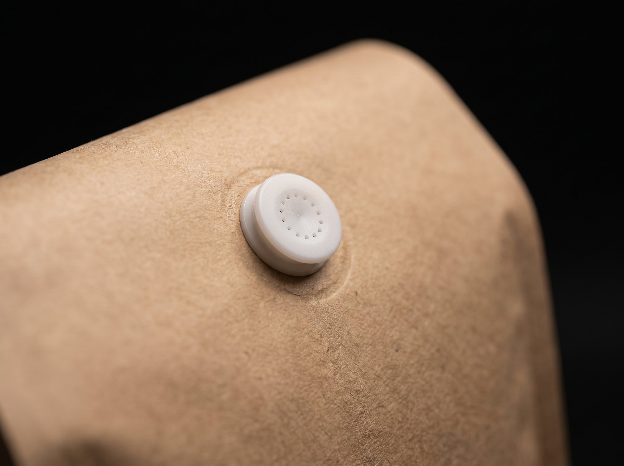 Close-up of a small white one-way degassing valve on the kraft face of a coffee bag.