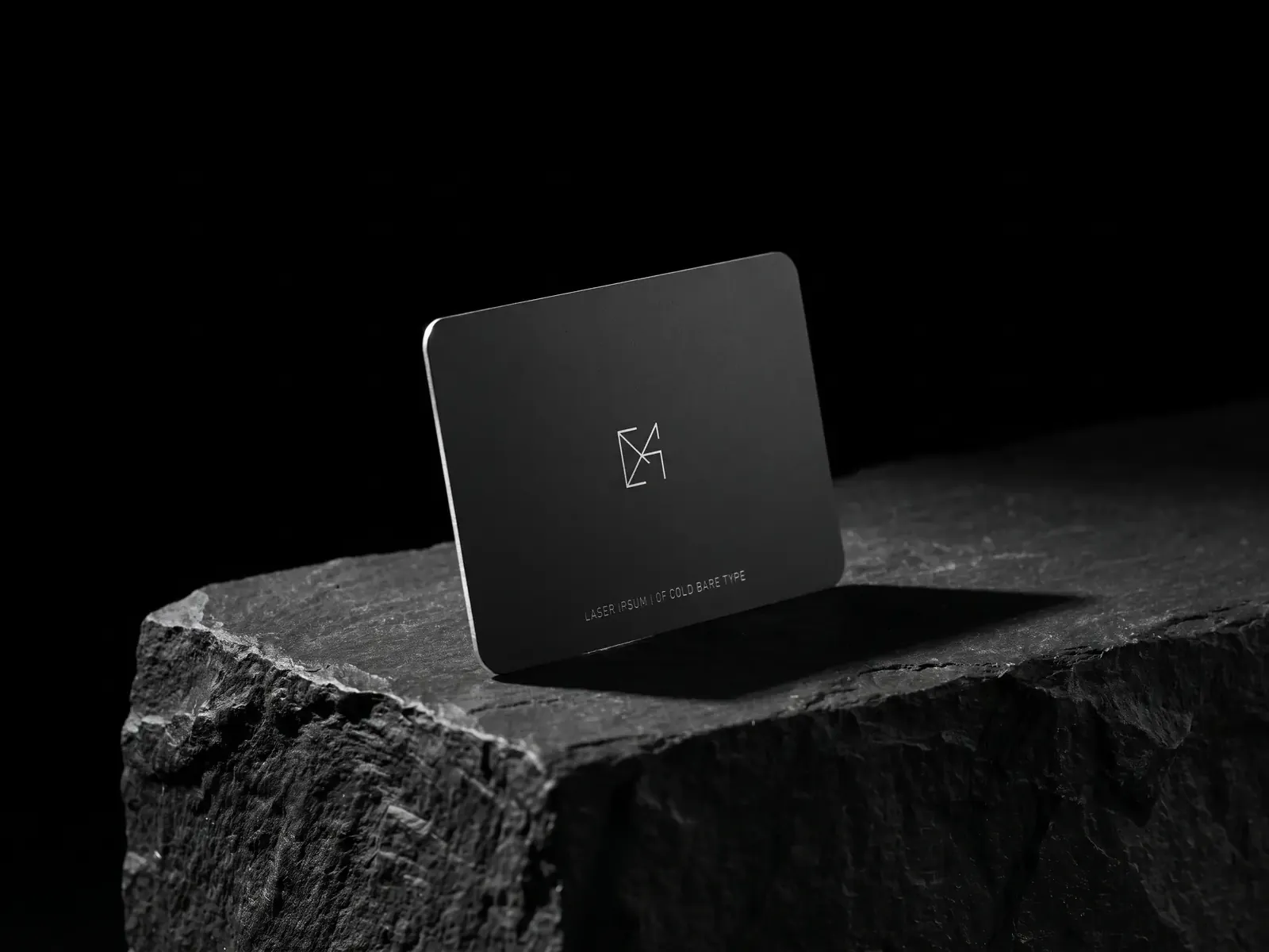 Matte black stainless steel business card with an engraved bright-steel monogram on a stone plinth