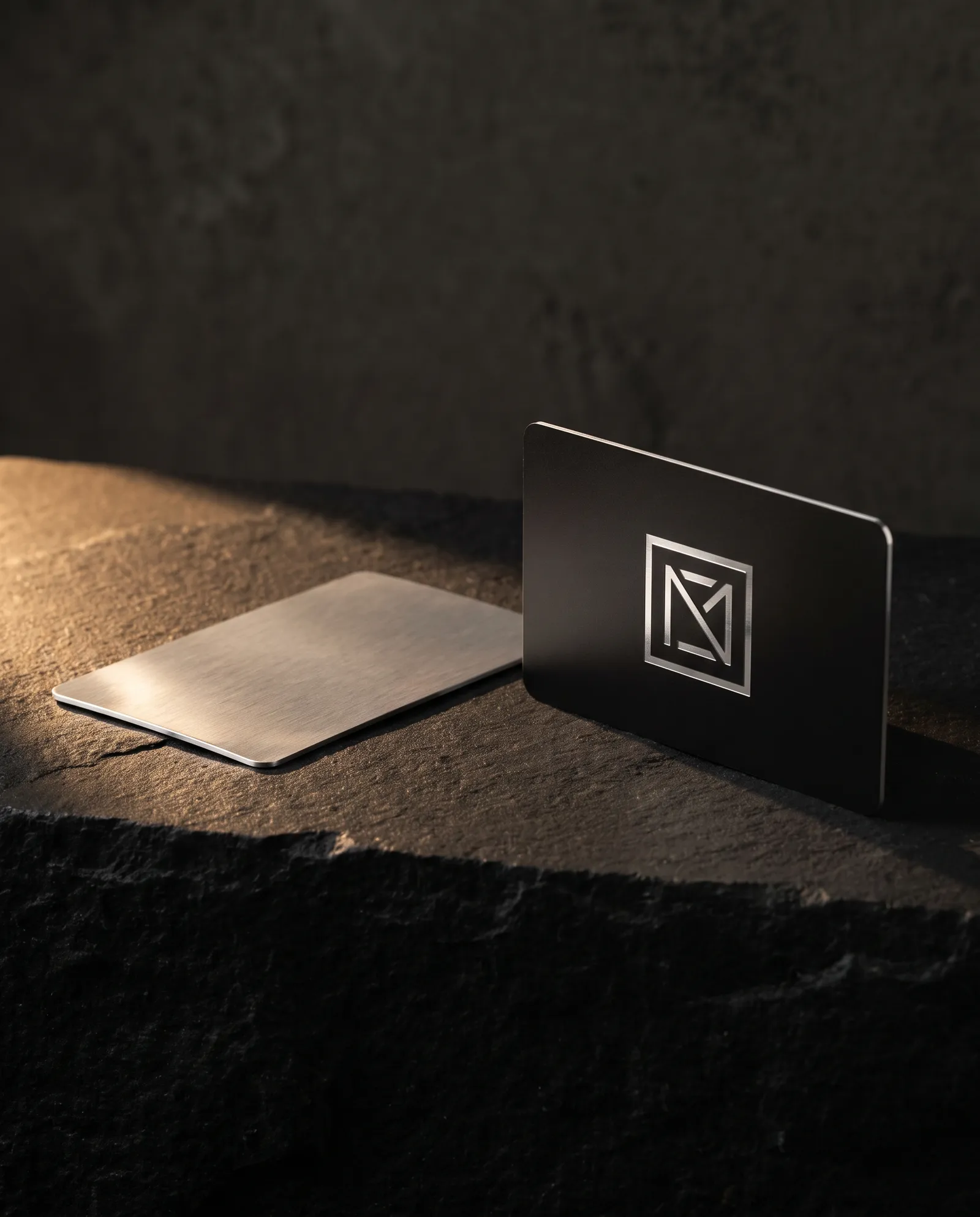 The cheapest metal business cards compared: a thin blank aluminum card beside a finished 0.5 mm black stainless business card with an engraved monogram