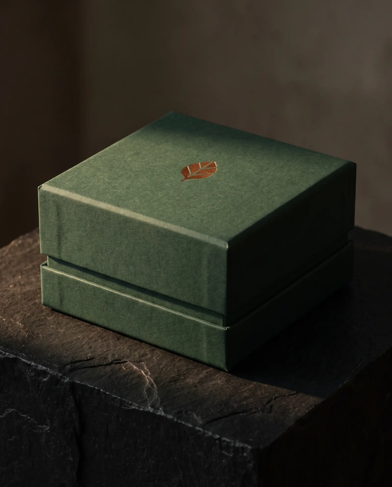 Closed forest-green uncoated two-piece rigid box with copper foil leaf on black stone