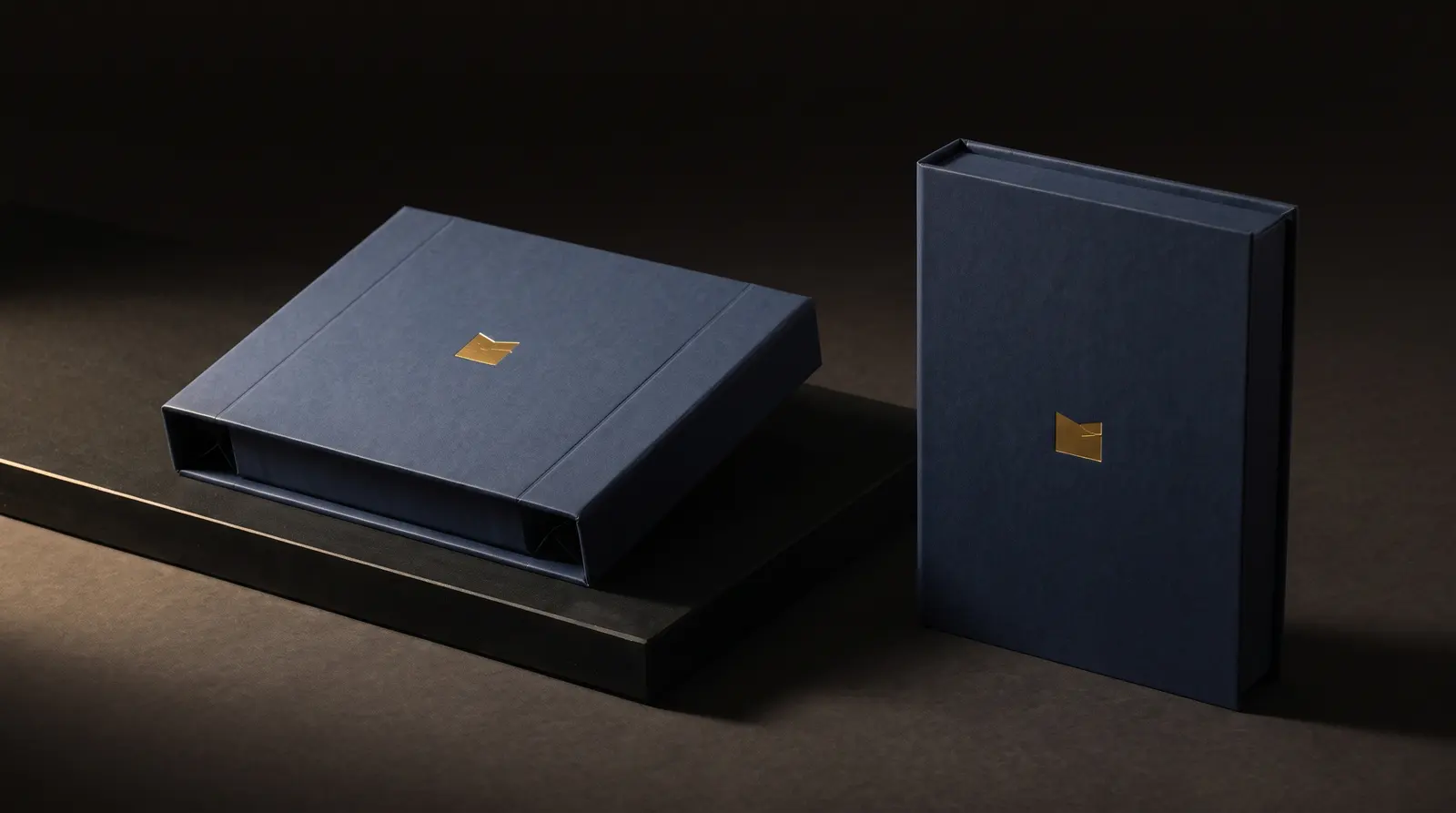 Navy collapsible magnetic box folded flat beside same box assembled, gold foil, black plinth
