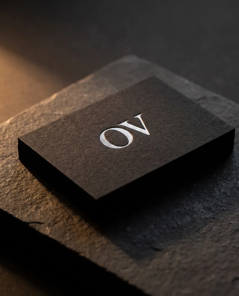 Black dyed-through cotton business card with matte silver foil OV monogram on black stone