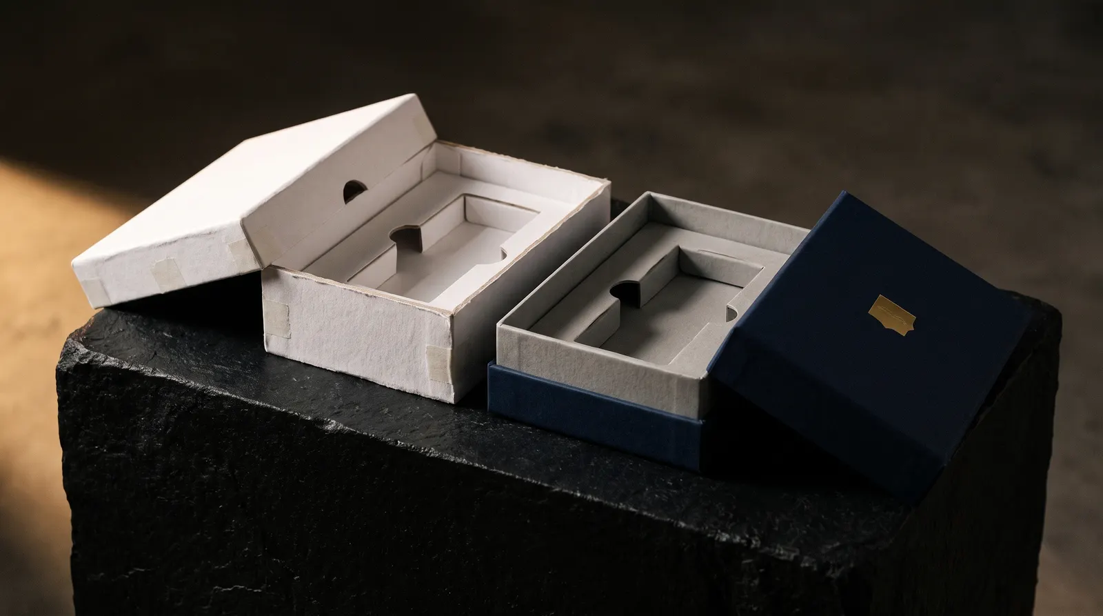 White unprinted rigid box prototype beside finished navy gold foil box with matching grey inserts