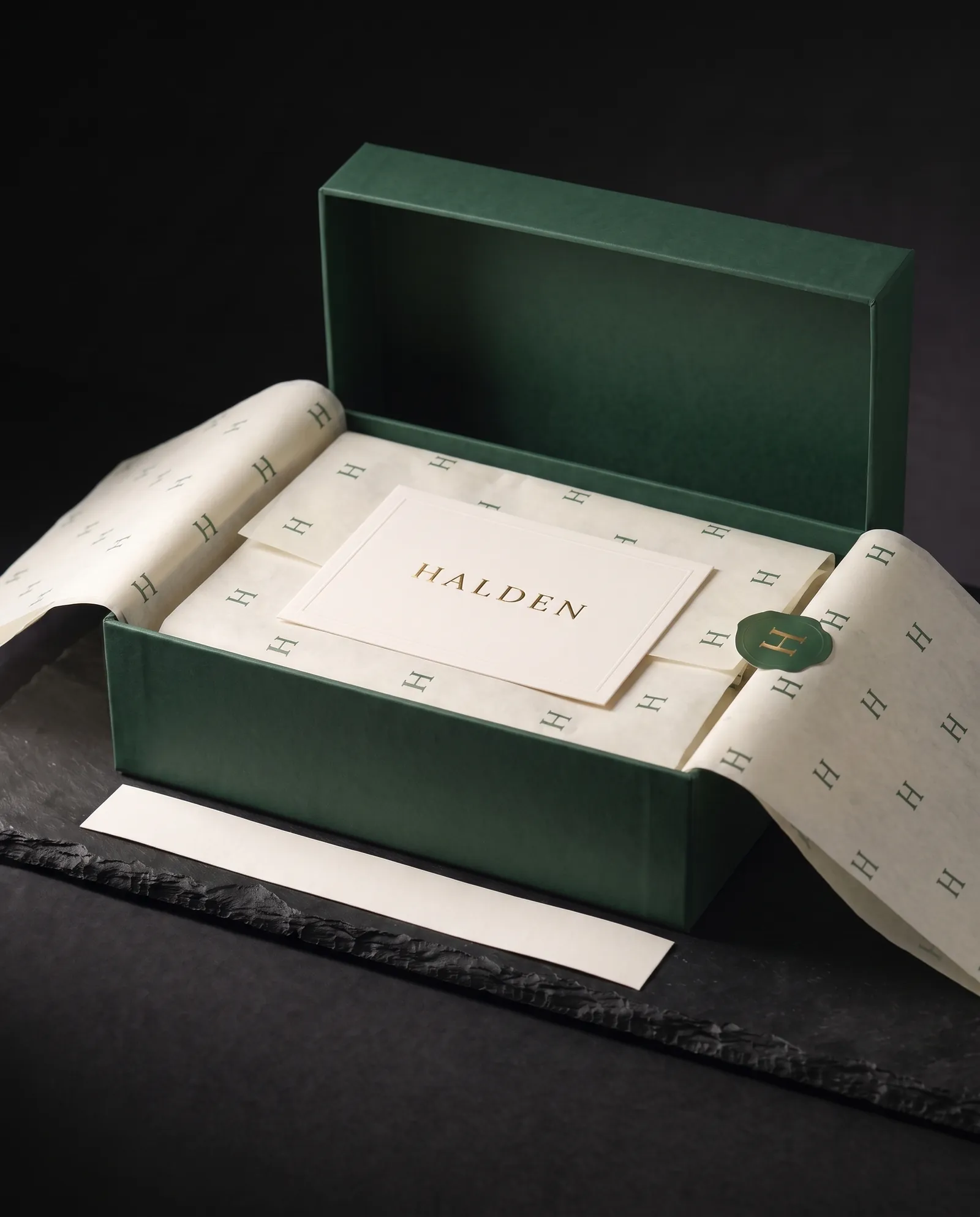 Printed tissue folded open to reveal an ivory cotton insert card with a gold foil wordmark