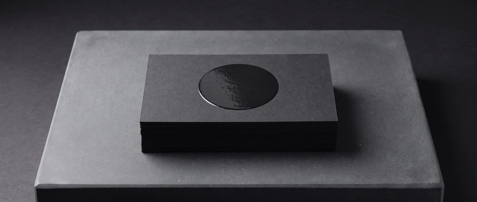 A raised gloss spot UV disc on black soft-touch, same colour, different surface.