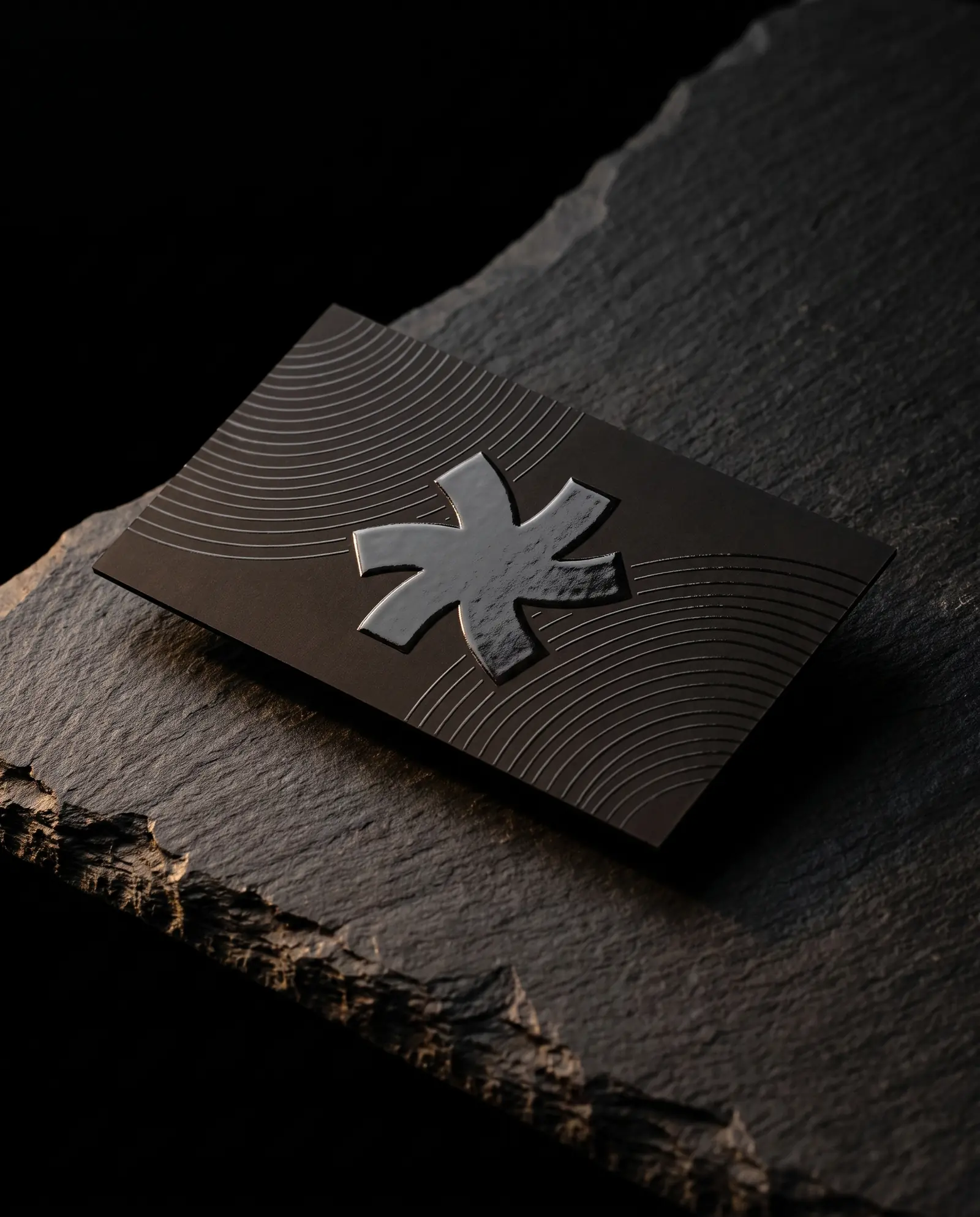 Black soft-touch business card with the Print Peppermint mark and fine arcs in raised clear spot UV, the domed gloss catching a warm raking light on black slate