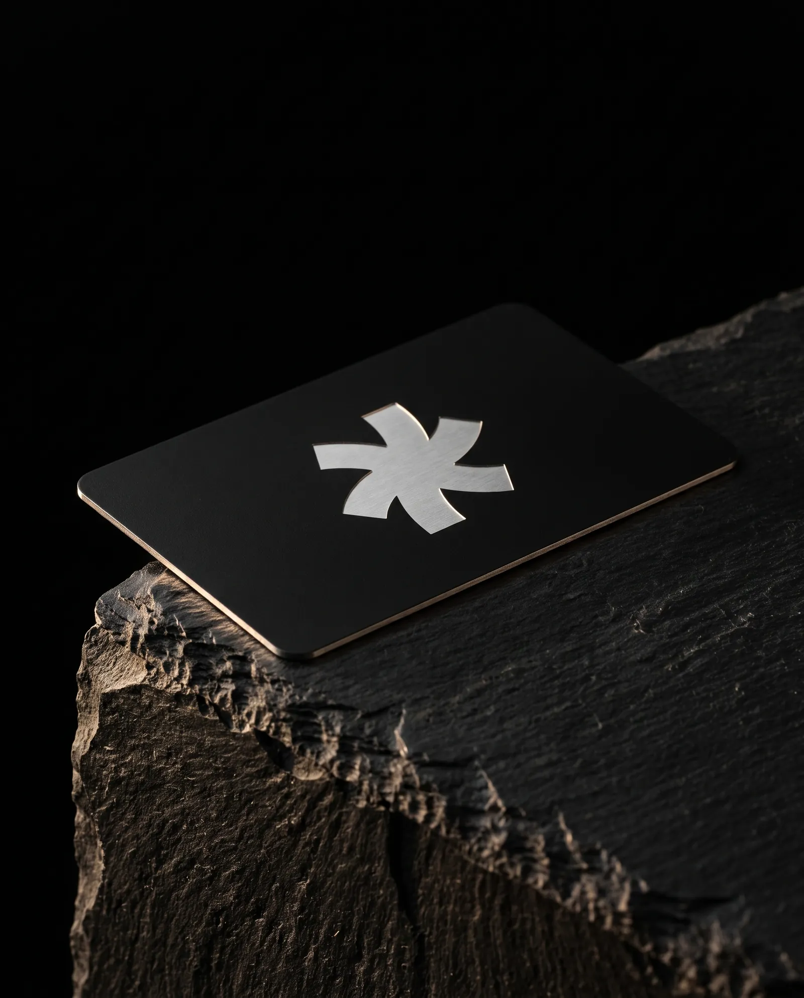 Matte black-coated steel business card with the Print Peppermint mark laser-etched to bright bare steel, on black slate