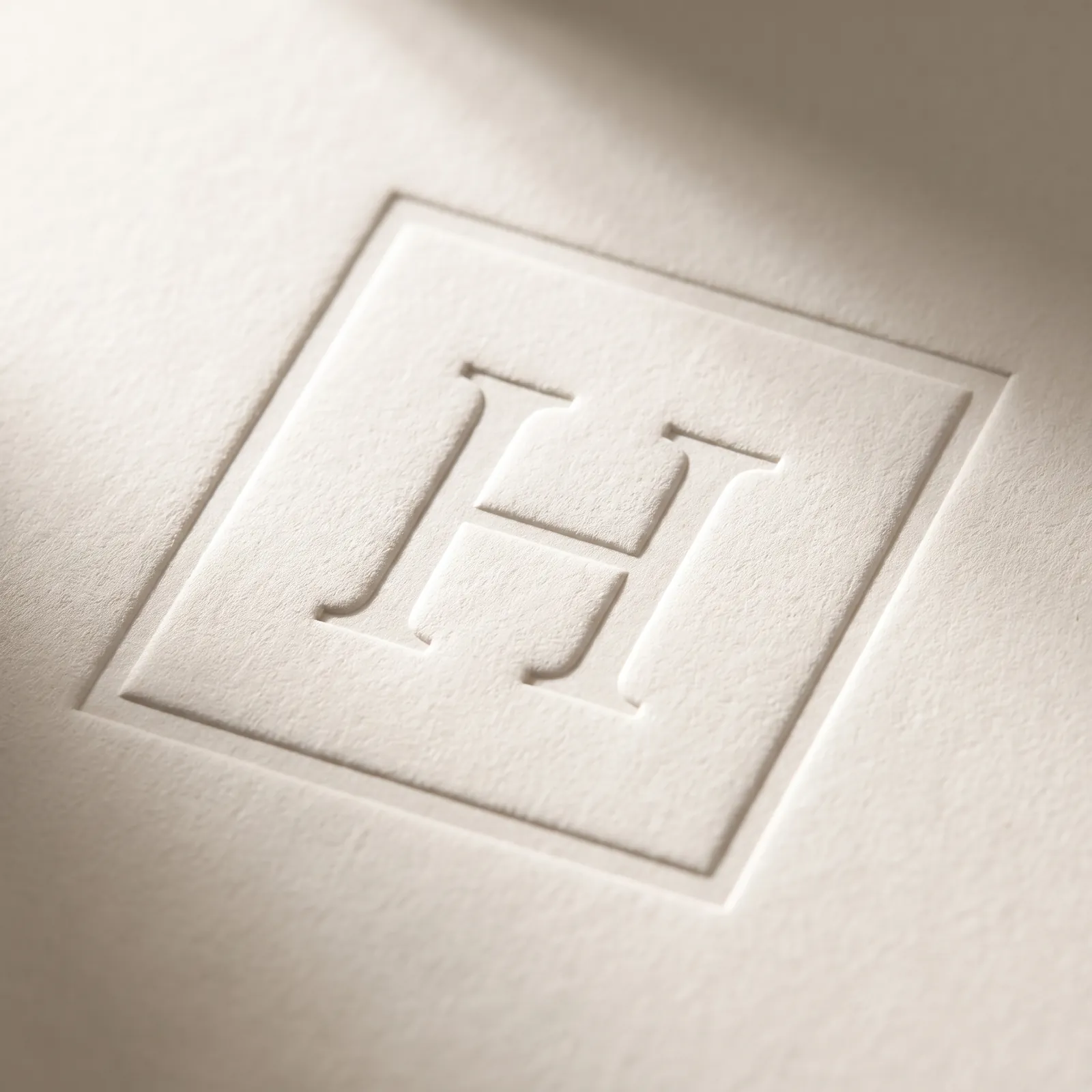 A blind pressed monogram and border in ivory cotton, read by shadow alone