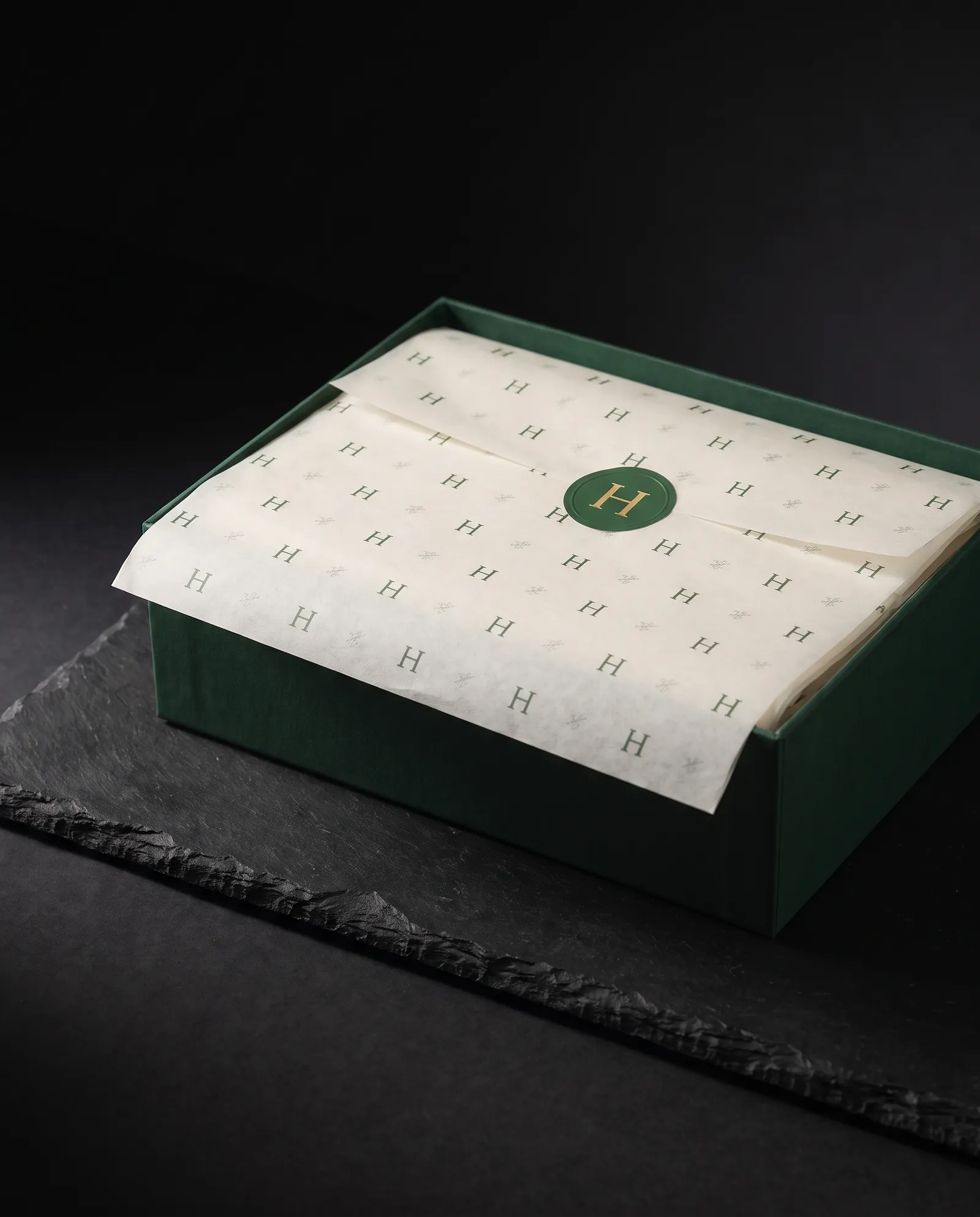 Ivory tissue printed with a small green monogram, folded into a green box and closed with a foil sticker seal