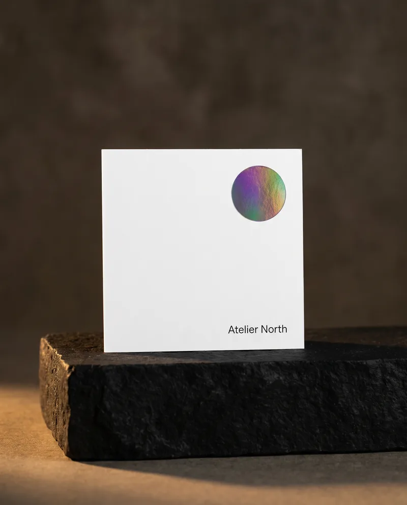 Square white business card with single holographic rainbow foil circle and black type on stone