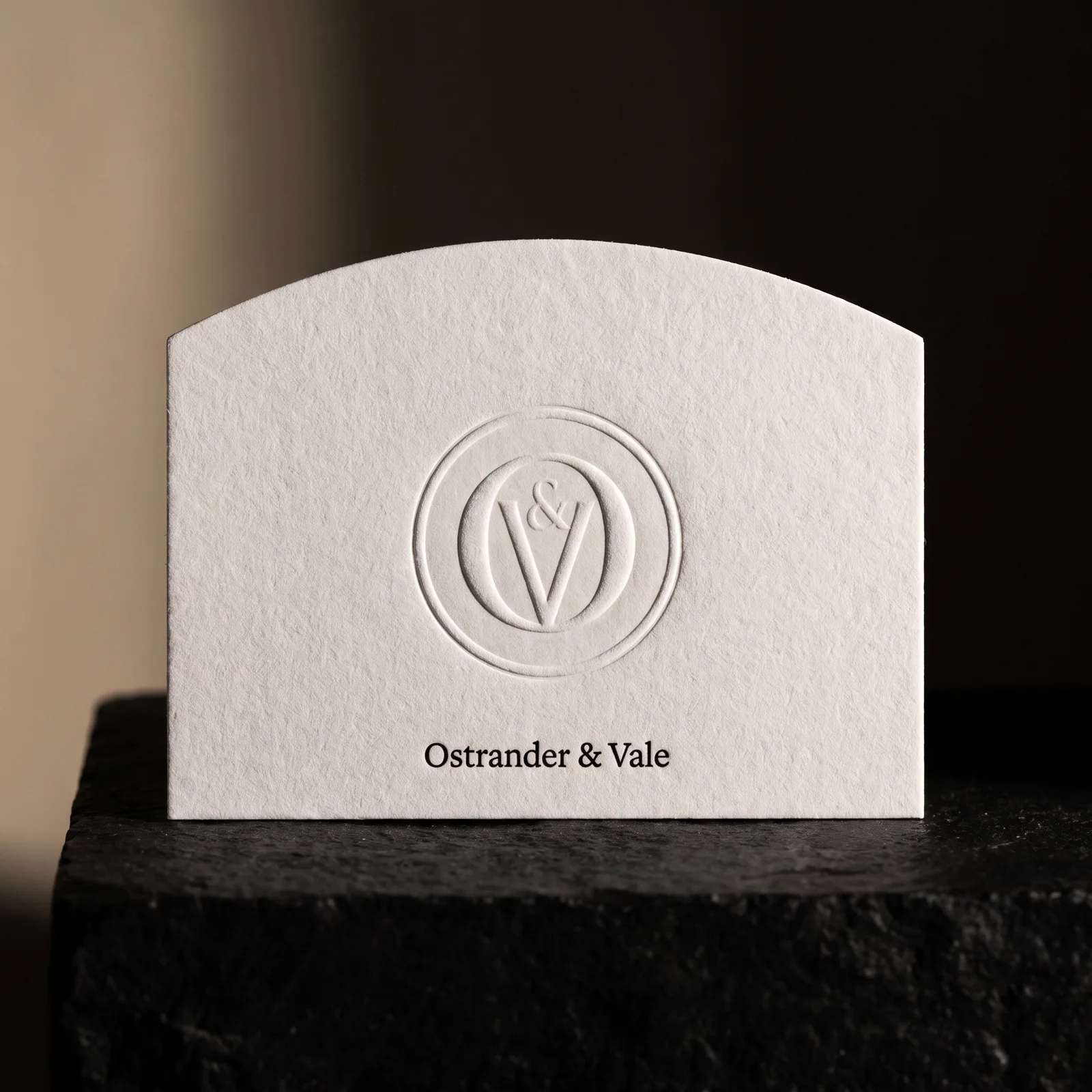 Arch-top die cut business card on white cotton with blind deboss emblem, black name