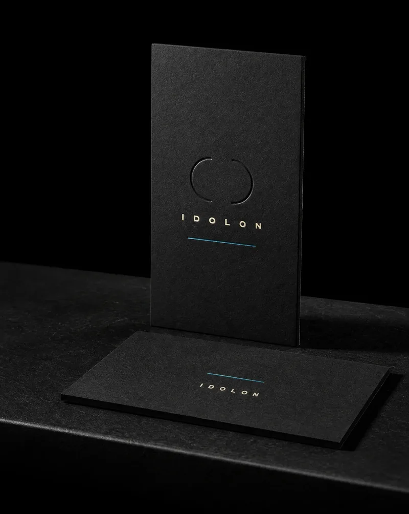 Black business card with a blind-debossed mark and metallic cyan foil, no printed ink