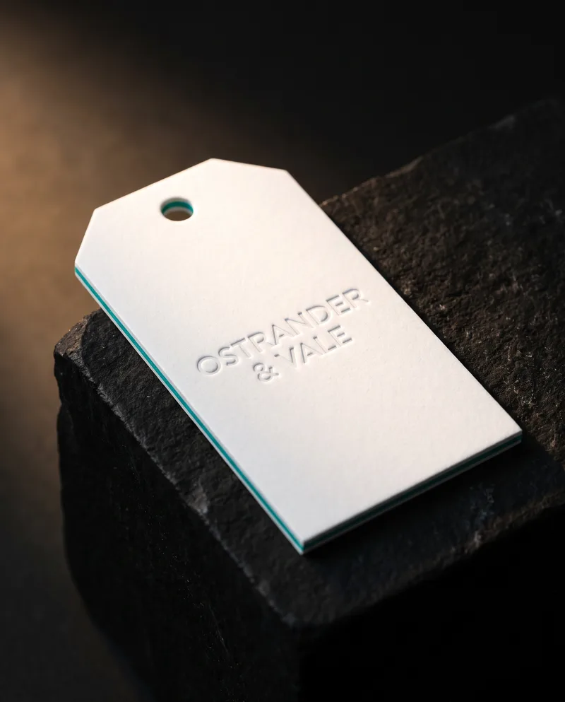 White cotton triplex swing-tag business card with teal core edge and blind emboss