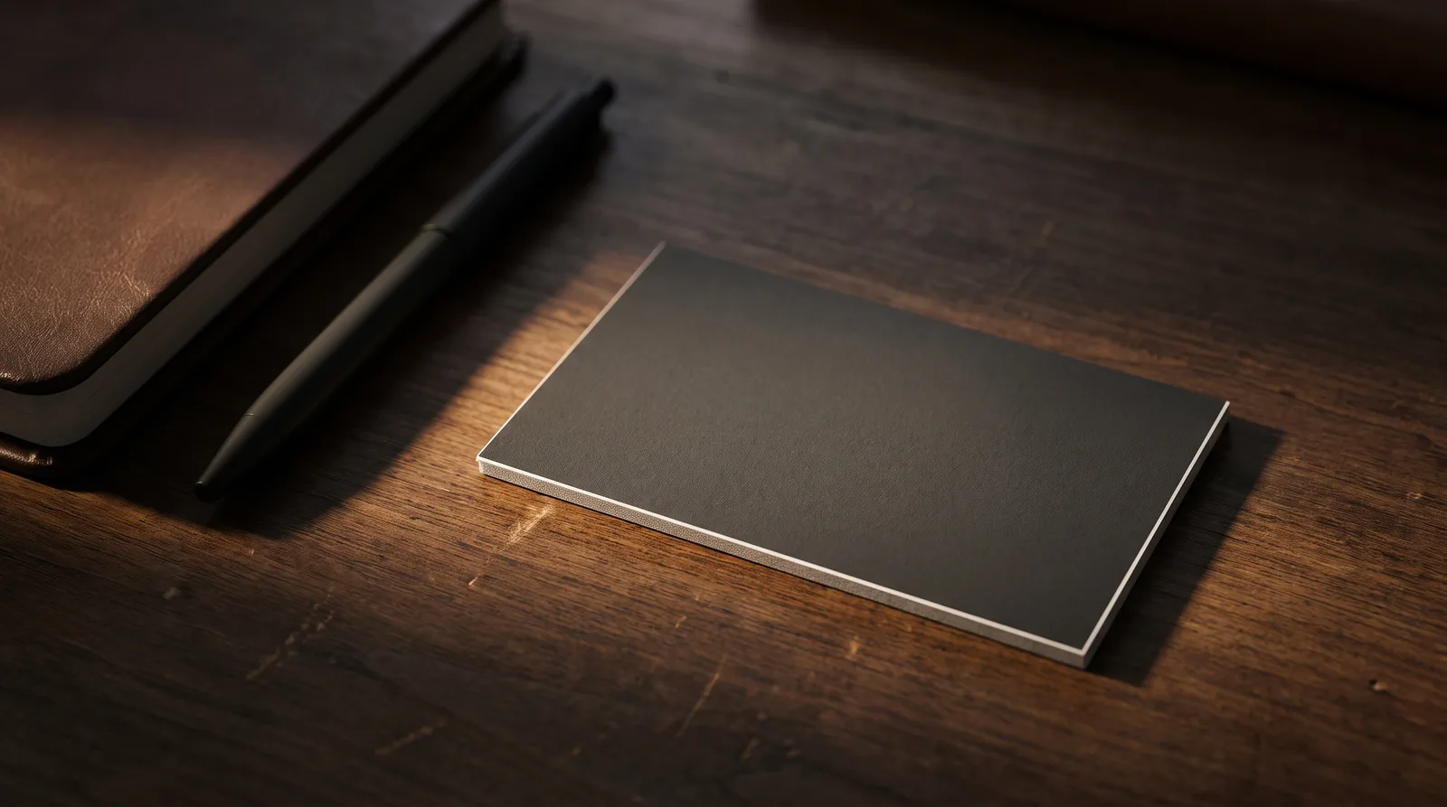 Charcoal soft touch business card on a walnut desk beside a leather notebook and pen
