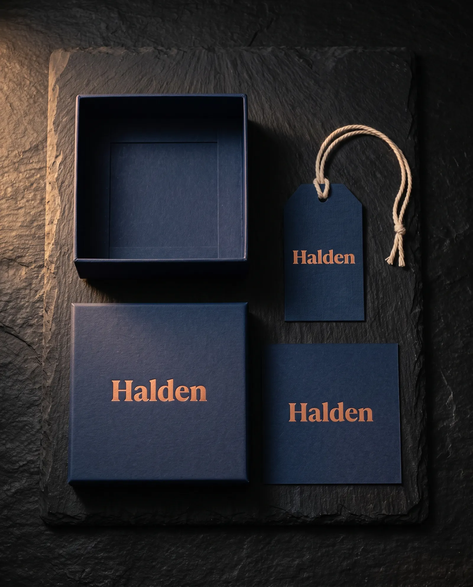 Navy rigid box, hang tag and insert card with matching copper hot-foil wordmark, top-down on stone
