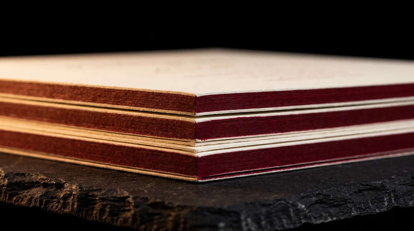 Two-ply cotton cards seen edge-on, showing the bonded layers and an oxblood painted edge.