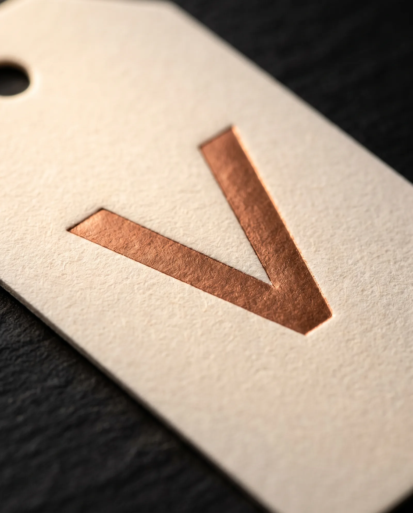 Close-up of a copper foil mark pressed into cream cotton, the edge of a drilled hole just in frame.