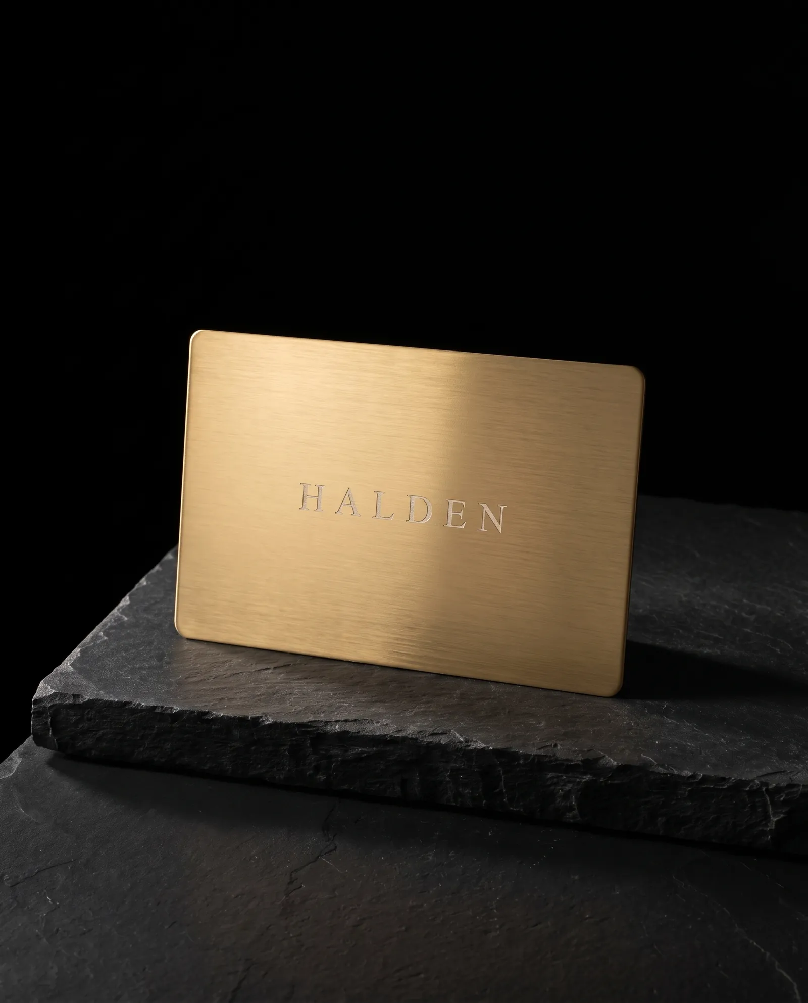 Brushed gold PVD stainless steel business card with an engraved wordmark showing silver steel